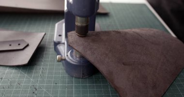 Deri malzemelerde delikler açmak için küçük basın araçları kullanan zanaatkârların yakın plan çekimleri, hassasiyet, işçilik ve el yapımı.