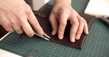 Close up of craftsman marking straight stitching line with divider tool on leather wallet. Step in handmade leatherworking process.