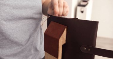 Artisan sewing leather manually using thread and needle fixed on wooden stitching pony. Detail of handmade leather crafting.
