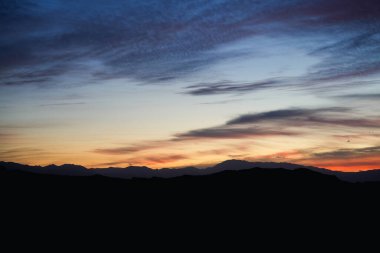 Gün batımında dağ siluetleri üzerinde sıcak kırmızı ve turuncu renkler. Huzurlu ve huzurlu doğal manzara.
