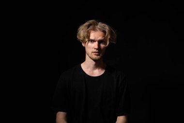 Siyah gömlekli bir adamın stüdyo portresi gergin ve endişeli görünüyor koyu renk düşük ayarlı aydınlatma altında güçlü bir kontrast altında.