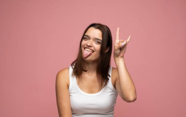 Neşeli kadın model, şakacı bir şekilde dil gösteriyor ve rock hareketleriyle stüdyoda eğlenceli bir ruh hali sergiliyor..