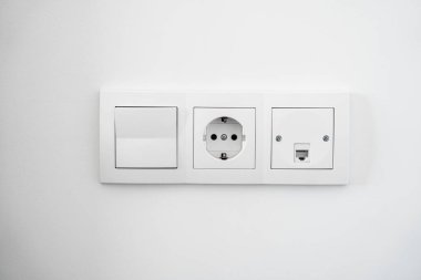 Pürüzsüz bir duvar yüzeyine yerleştirilmiş modern beyaz elektrik şalterleri ve soketleri temiz iç dekorasyon ve fonksiyonel tasarım sergiliyor..