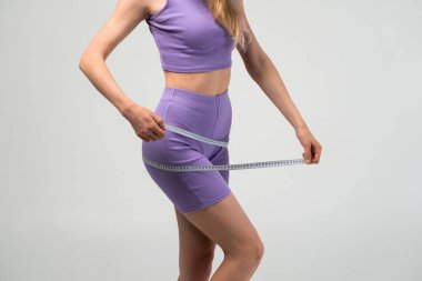 Leylak rengi etek giyen bayan sporcu ölçüm bandı, fitness motivasyonu ve sağlıklı vücut yaşam tarzı konseptiyle kalçalarını ölçüyor..