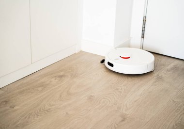 Robotik süpürge kabinin yanındaki ahşap zemin boyunca hareket eder ve modern bir ev içinde akıllı otomatik temizlik yapar..