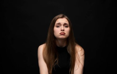 Uzun saçlı, esmer, duygusal ifadeler sergileyen ve dramatik bir ruh hali içinde üzgün bir genç kadının stüdyo portresi.