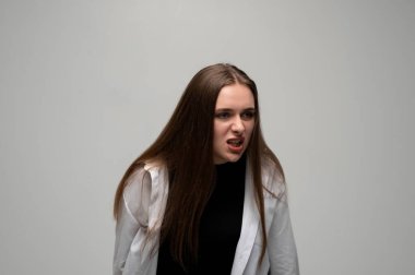 Basit bir gri stüdyoda yakalanmış, agresif ve kızgın bir ifadeyle öne eğilmiş genç bir kadının portresi..