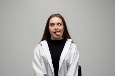 Komik bir ifade takınırken gözlerini şaşı yapıp dilini uzatan genç bir kadının oyuncu stüdyo portresi..