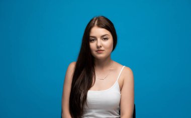 Temiz ve modern bir stüdyo portresi genç bir kadının sakin bir şekilde canlı mavi bir arka plana poz vererek yeni ve parlak bir görsel hava yaratıyor..