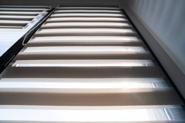 Pencere üzerindeki çizgili panjurların dikey görüntüsü ve güneş ışığı minimum modern uzayda geometrik desenler yaratıyor.