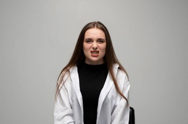 Genç bir kadının portresi hırıldıyor ve dişlerini gösteriyor. Gerginliğini ve öfkesini gri bir arka planda ifade ediyor..