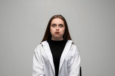 Yanaklarını şişiren ve gözlerini büyüten genç bir kadının oyuncu stüdyo portresi komik bir yüz ifadesi yaratıyor..