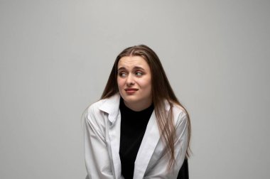 Stüdyo portresi. Gri bir arka planda kafa karışıklığı ve belirsizliği ifade eden genç bir kadın.