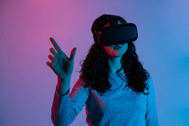 Kadın VR kullanıcısı, stüdyoda canlı mavi ve kırmızı neon ışıkta durarak sanal bir ortamla etkileşime geçmek için iki elini de kaldırır..