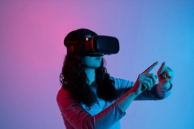 Bir kadın, neon renklerle aydınlatılmış bir VR kulaklık takarken anlamlı el hareketleri kullanarak sanal bir dünyayı keşfediyor..