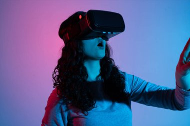 Bir kadın, canlı pembe ve mavi neon ışıklar hareketini ve tepkisini ön plana çıkarırken, bir VR kulaklığı takarken hayranlığını ifade eder..