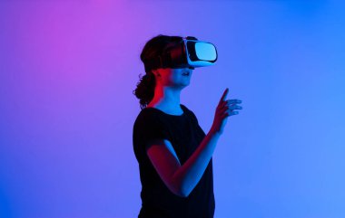 Sanal içerikle etkileşime geçmek için beyaz kulaklık takan kadın VR kullanıcısı, mavi ve pembe neon stüdyo ışıklandırmasıyla ışıklandırılıyor..