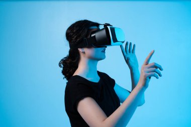 Sanal kontrolleri ve hareket arayüzünü keşfeden, mavi arkaplandaki dijital ortamla etkileşime geçmek için VR kulaklık takan bir kadın
