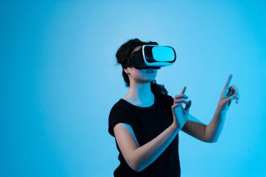 Sanal kontrolleri ve hareket arayüzünü keşfeden, mavi arkaplandaki dijital ortamla etkileşime geçmek için VR kulaklık takan bir kadın