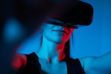 Sanal gerçeklik kulaklığı takan bir kadın, dramatik kırmızı ve mavi ışıklarla çevrili dijital bir ortama bağlanır..