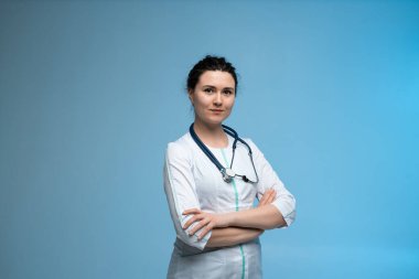 Steteskopla tıbbi üniforma giyen gülümseyen bir kadın doktorun portresi mavi arka plana güvenle poz vererek modern sağlık hizmetleri profesyonelliğini gösteriyor.