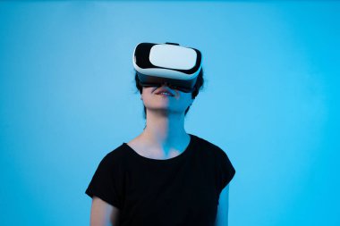 VR kulaklık takan bir kadın mavi arka planda sanal bir arayüzle etkileşime giriyor ve dijital teknoloji deneyimini keşfediyor.