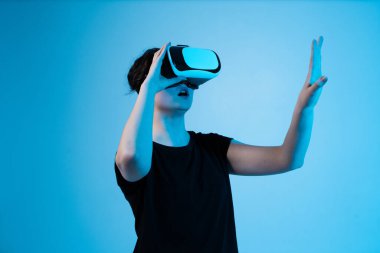 Sanal kontrolleri ve hareket arayüzünü keşfeden, mavi arkaplandaki dijital ortamla etkileşime geçmek için VR kulaklık takan bir kadın