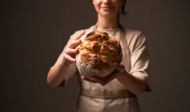Becerikli bir fırıncı, otantik zanaatkarlığı, doğal malzemeleri ve sanatsal pişirme geleneğini vurgulayan, rustik bir ekmek somunu tutar..