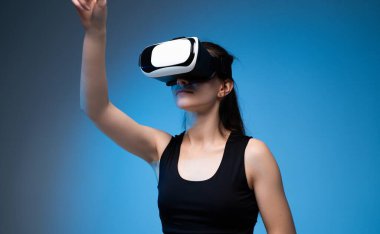 Sanal bir çevreyle etkileşim halinde olan VR kulaklıklı bir kadın kolunu kaldırıyor. Modern dijital teknoloji ve sanatsal deneyim kavramı.