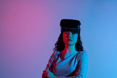 Kadın VR kullanıcısı, stüdyo ortamında yumuşak mavi ve pembe neon tonlarıyla aydınlatılmış, alnında kulaklıkla hareketsiz duruyor..