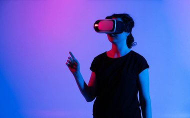 Sanal gerçeklik kulaklığı takan ve el hareketi yaparak dijital alanla etkileşime giren kadın kullanıcı. Etkileyici teknoloji, geleceksel iletişim, yenilik, eğlence ve sanal etkileşim kavramı.