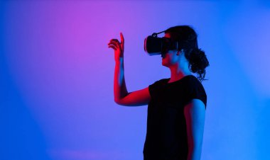 Neon Stüdyo ışıklandırmasında sanal gerçeklik kulaklığı takan bir kadının yan görünümü. Çevrimiçi dijital deneyim, fütüristik teknoloji, yenilik, simülasyon ve modern eğlence kavramı.