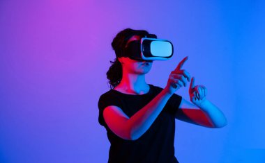 VR kulaklık takan ve el hareketleri kullanarak görünmez bir dijital arayüzle etkileşime geçen kadın kullanıcı. Fotokopi alanı ve neon ışıklandırması ile gelecek teknolojisi kavramı.