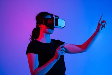 VR kulaklık takan ve sanal bir arayüzü işaret eden bir kadının yan görüntüsü. Kapsamlı etkileşim ve gelecekteki dijital teknoloji kavramı.