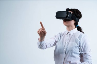 Kadın kullanıcı VR kulaklık takıyor ve parmak hareketleriyle sanal içeriği seçiyor. Temiz beyaz arka planda gelecekçi dijital etkileşim kavramı.