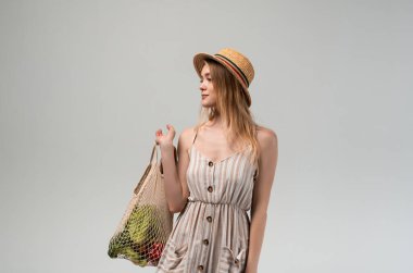 Ayakta duran ve elinde sebze ve ekmek dolu bir alışveriş çantası tutan genç bir kadın. Sağlıklı beslenme, sürdürülebilir yaşam tarzı, organik bakkaliye ve bilinçli tüketici tercihleri kavramı.