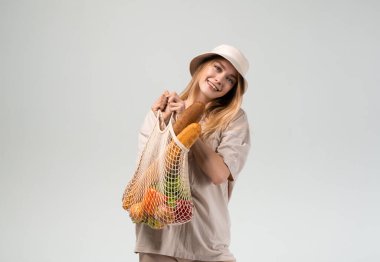 Gülümseyen ve elinde alışveriş torbası tutan genç bir kadın. Çevre dostu alışveriş alışkanlıkları, sürdürülebilir yaşam tarzı ve sağlıklı gıda tüketimi.