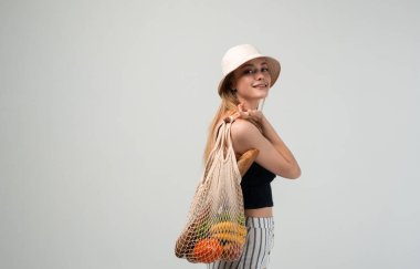 Gülümseyen ve poz veren genç bir kadın. Taze ürünlerle dolu bir alışveriş poşeti. Sürdürülebilir alışveriş, sıfır atık yaşam tarzı ve sorumlu tüketim kavramı.