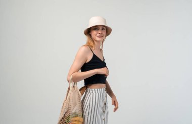 Elinde taze meyve, sebze ve ekmek, sürdürülebilir alışveriş ve eko yaşam tarzı konseptiyle yeniden kullanılabilir ağ çantası tutan gülümseyen genç kadın.