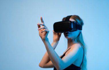 VR kulaklıklı kadın, dijital çevreyi anlamlı el hareketleriyle keşfediyor. Sanal gerçekliği, yeniliği ve etkileşimi temsil eden stüdyo portresi.