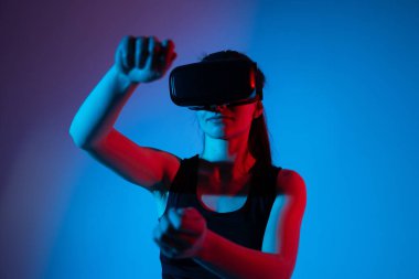 VR kulaklık takan ve sanal ortamı kontrol etmek için kapalı el hareketi yapan bir kadın. Hareket takip, hareket kontrolü, donanımlı teknoloji ve dijital etkileşim kavramı.