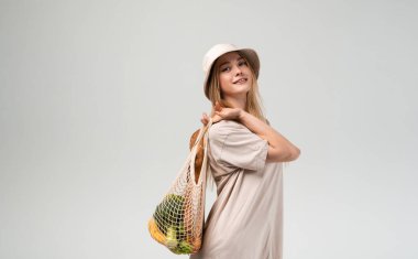 Omzunda alışveriş poşeti taşıyan gülümseyen genç bir kadın. Sürdürülebilir alışveriş, çevre dostu yaşam tarzı, sağlıklı gıda seçenekleri ve modern tüketici alışkanlıkları.