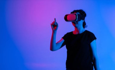 Sanal gerçeklik kulaklığı takan ve sanki sanal arayüzle etkileşim içindeymiş gibi yukarıya bakan bir kadın. Kapsamlı teknoloji kavramı, dijital etkileşim, geleceksel arayüz ve modern deneyim.