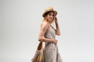 Genç bir kadın, içi taze sebze ve ekmekle dolu yeniden kullanılabilir bir alışveriş çantası taşırken yürüyor. Sürdürülebilir market alışverişi, sağlıklı yaşam tarzı, bilinçli tüketim ve çevre dostu alışkanlıklar kavramı.