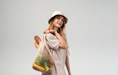 Yeniden kullanılabilir bir alışveriş çantasıyla poz veren genç bir kadın. Sürdürülebilir market alışverişi, eko yaşam tarzı, sağlıklı beslenme ve bilinçli tüketici davranışı.