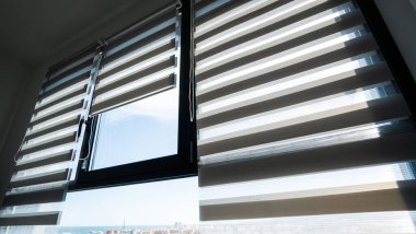 Çağdaş kentsel bir iç mekanda doğal gün ışığını filtreleyen saf ve donuk kumaş katmanlarını değiştirerek, daire penceresindeki modern zebra tekerlekli perdelerin yakın çekimi..