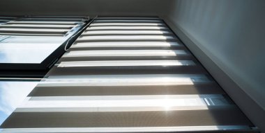 Gündüz paten sürüşünün iç ayrıntıları geniş penceredeki katmanlı kumaş şeritlerin temiz ve modern bir apartman ortamında güneş ışığını kontrol ettiğini gösteriyor..