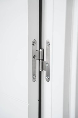 Beyaz iç kapıya monte edilmiş paslanmaz çelik menteşenin ayrıntılı görüntüsü, temiz çizgiler, hassas donanım ve modern iç mimari tasarım ve inşaat kalitesi vurgulanıyor..