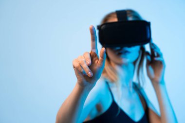 Genç kadın, görünmez bir dijital arayüzle etkileşime girerken sanal gerçekliği deneyimliyor. Bu resim ortak bir VR teması, daldırıcı teknoloji, kullanıcı deneyimi, yenilik ve gelecekteki dijital etkileşimi göstermektedir..