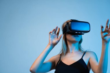 Sanal gerçeklik deneyimi, VR kulaklık takan ve el hareketleriyle hareket eden bir kadın. Oyun, yenilik, metaevren ve etkileşimli medya için gelecekçi dijital teknoloji kavramı.